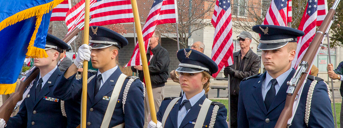 ROTC students standing at attention holding flags and guns
