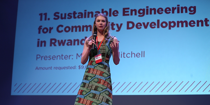 Presenter on stage with a PowerPoint presentation behind her