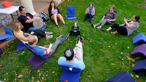  Students sitting outside in a circle, one with drum. 