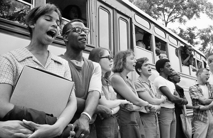 Civil rights activists holding hands and singing next to a bus