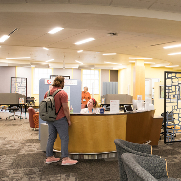 Student with backpack checks in for an appointment at the front desk of the Howe Writing Center.