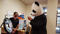 Tony Kinne standing next to a wheel of fortune type wheel and a person in a panda outfit