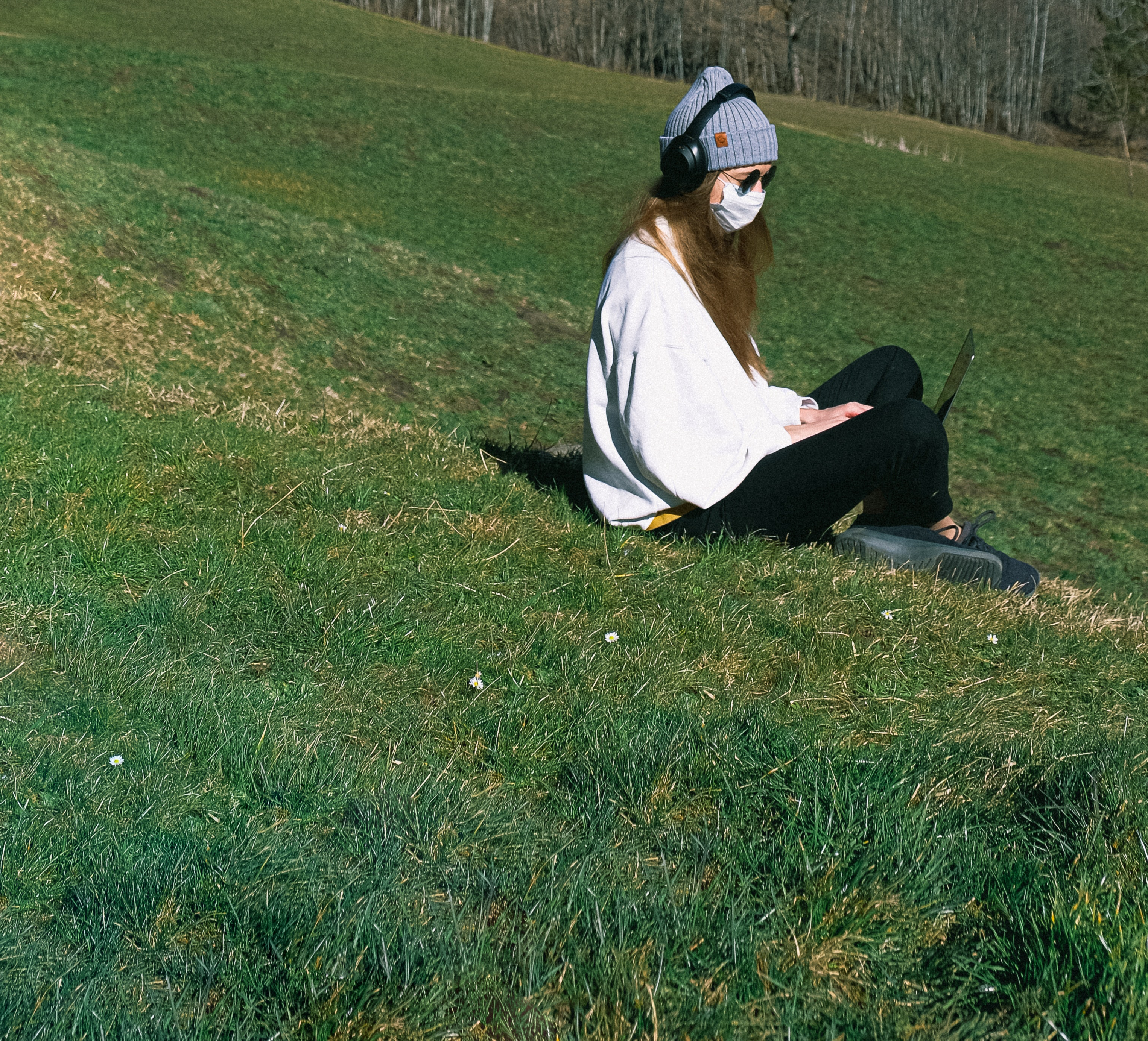 Student wearing a mask and sitting on the grass Using her Laptop