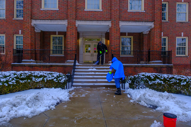 Two Miami University employees clear the steps of Roudebush Hall after a recent snowfall.. 