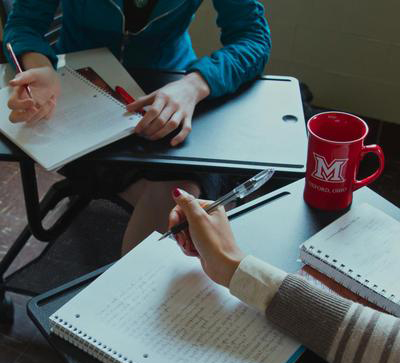 student hands with pens at a desk 