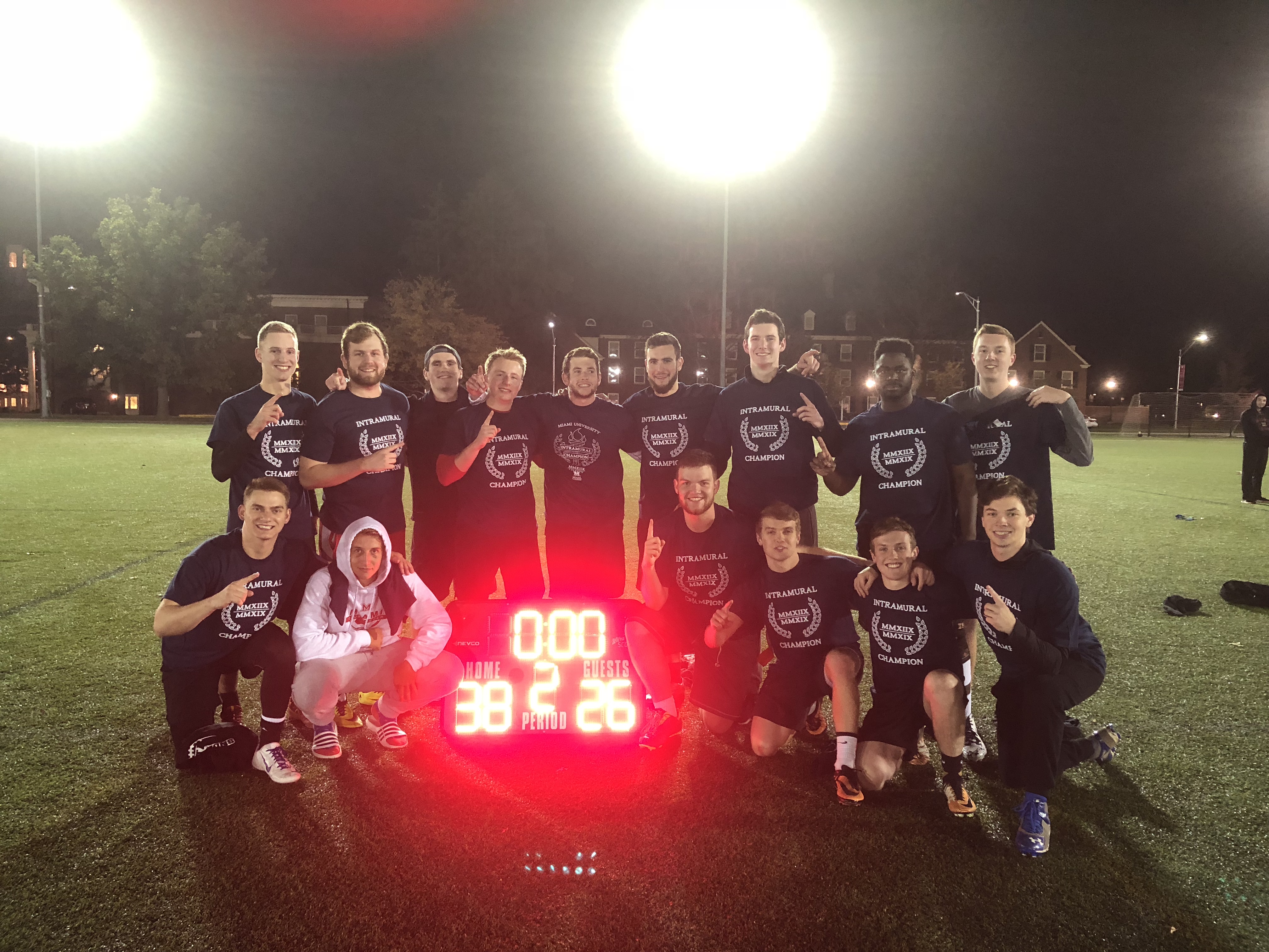 Champion flag football team stands around scoreboard to celebrate their victory.