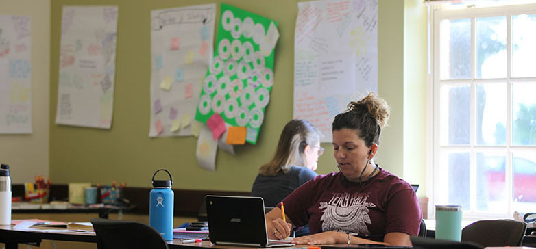 Teacher seated and working on a laptop in an art-filled classroom