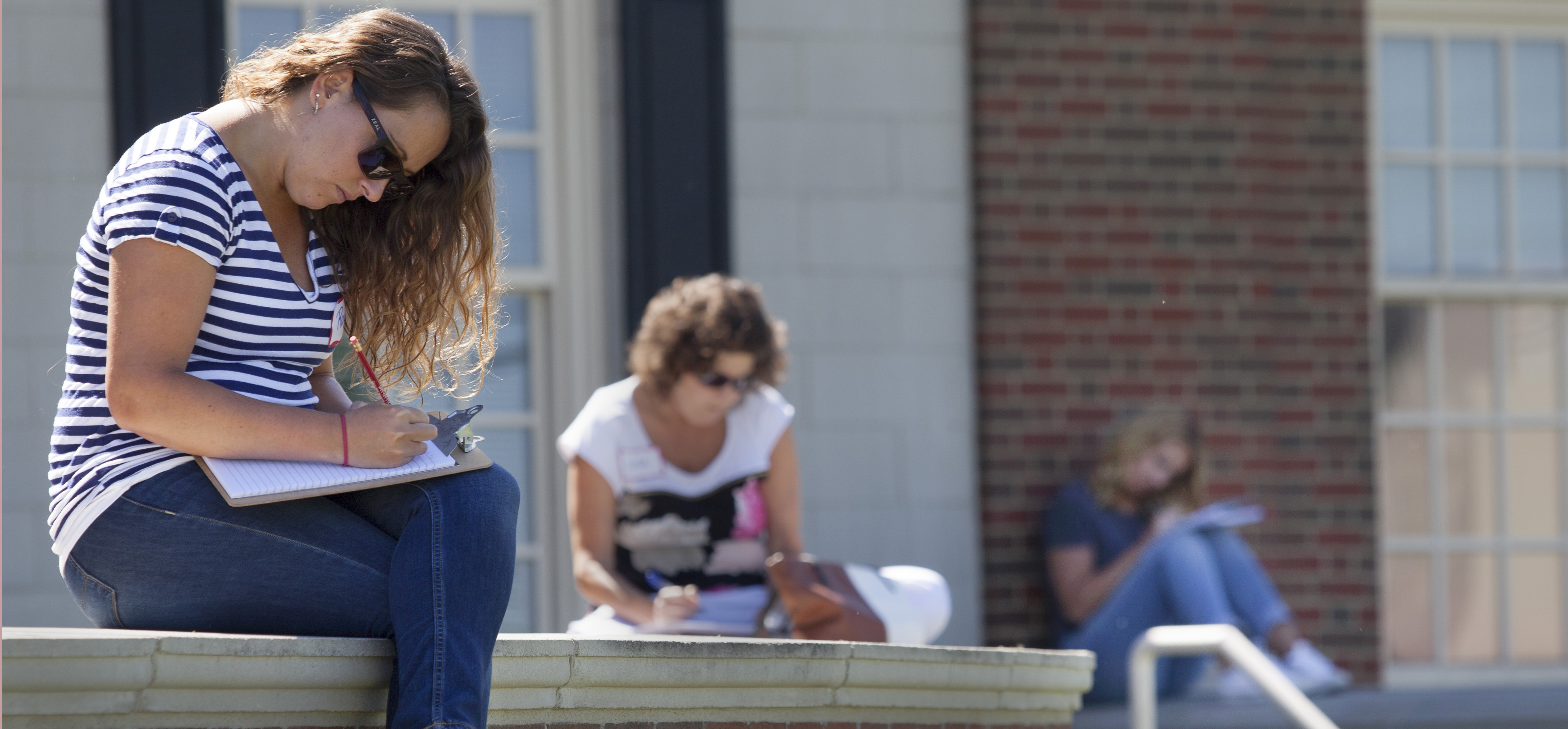 Students seated on a brick wall, writing in journals