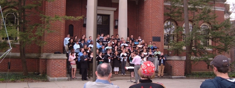 A choral group singing in front of Alumni Hall