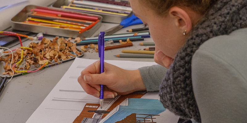 A woman leans in close to a drawing that she is working on
