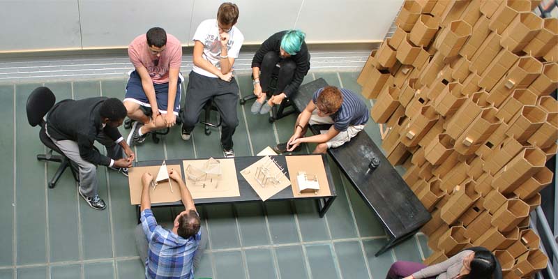  A birdseye view of students and faculty discussing sketches and models in the atrium