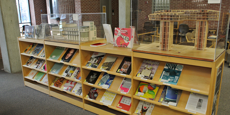 Architectural models are displayed on top of a low library shelf