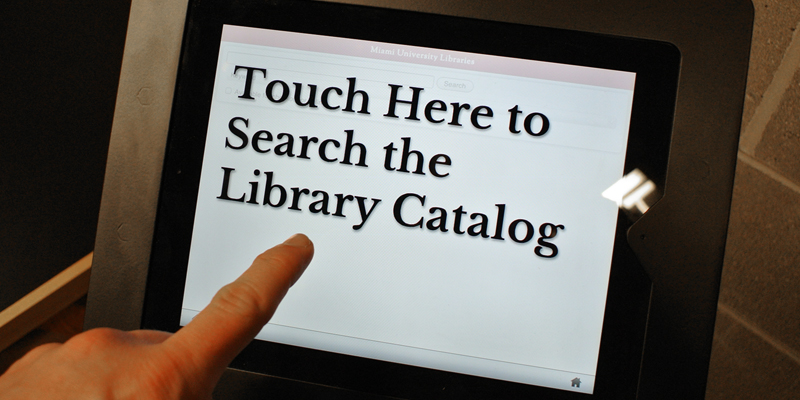 A library touchscreen with a pointing finger. Text: Touch here to search the library catalog