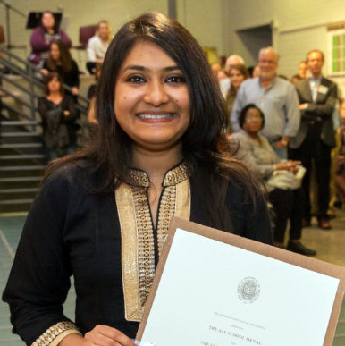 A smiling student holds a framed award certificate