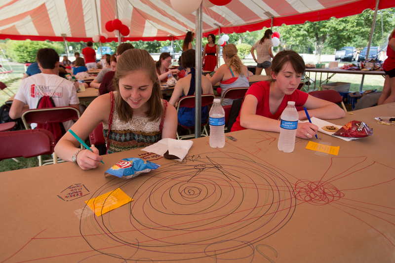  Students scribble on butcher block sheets at a table under the tent at the Lawn Party