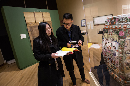 Two students stand before an artwork and consult a booklet