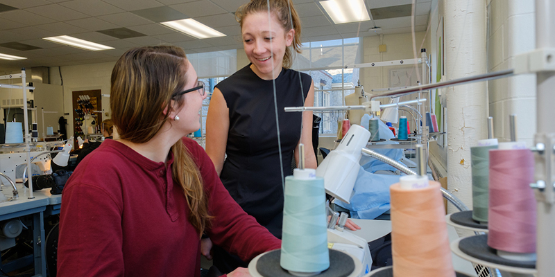 Two fashion students chat near colorful spools of thread