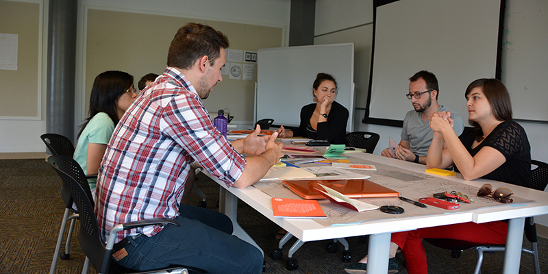 Experience Design students meet around a table, with materials spread around them.