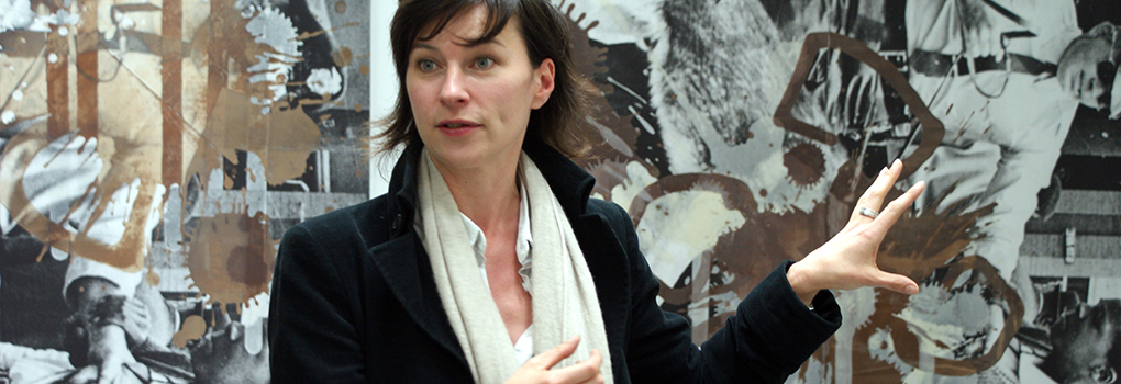 A museum curator delivering a talk as she gestures toward an artwork