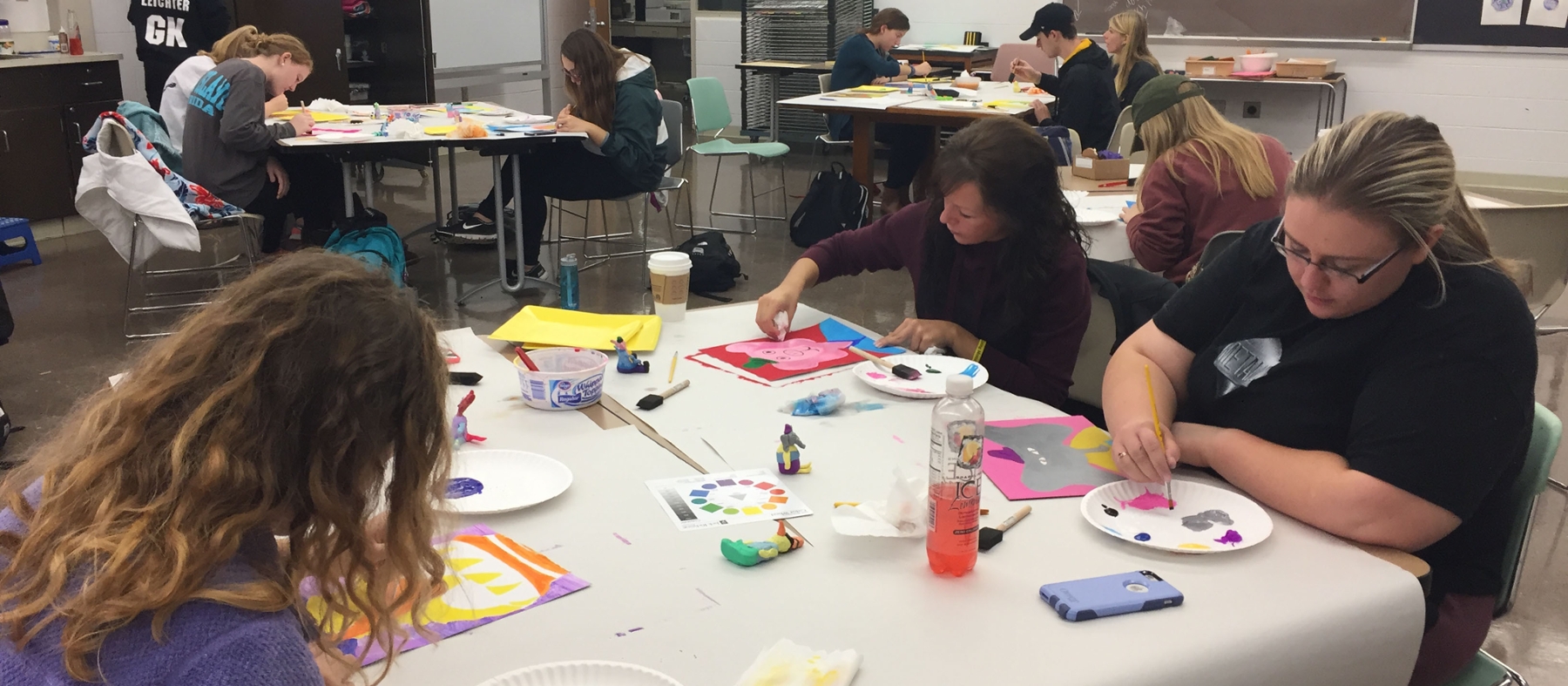 Student teachers and children work on art projects at tables