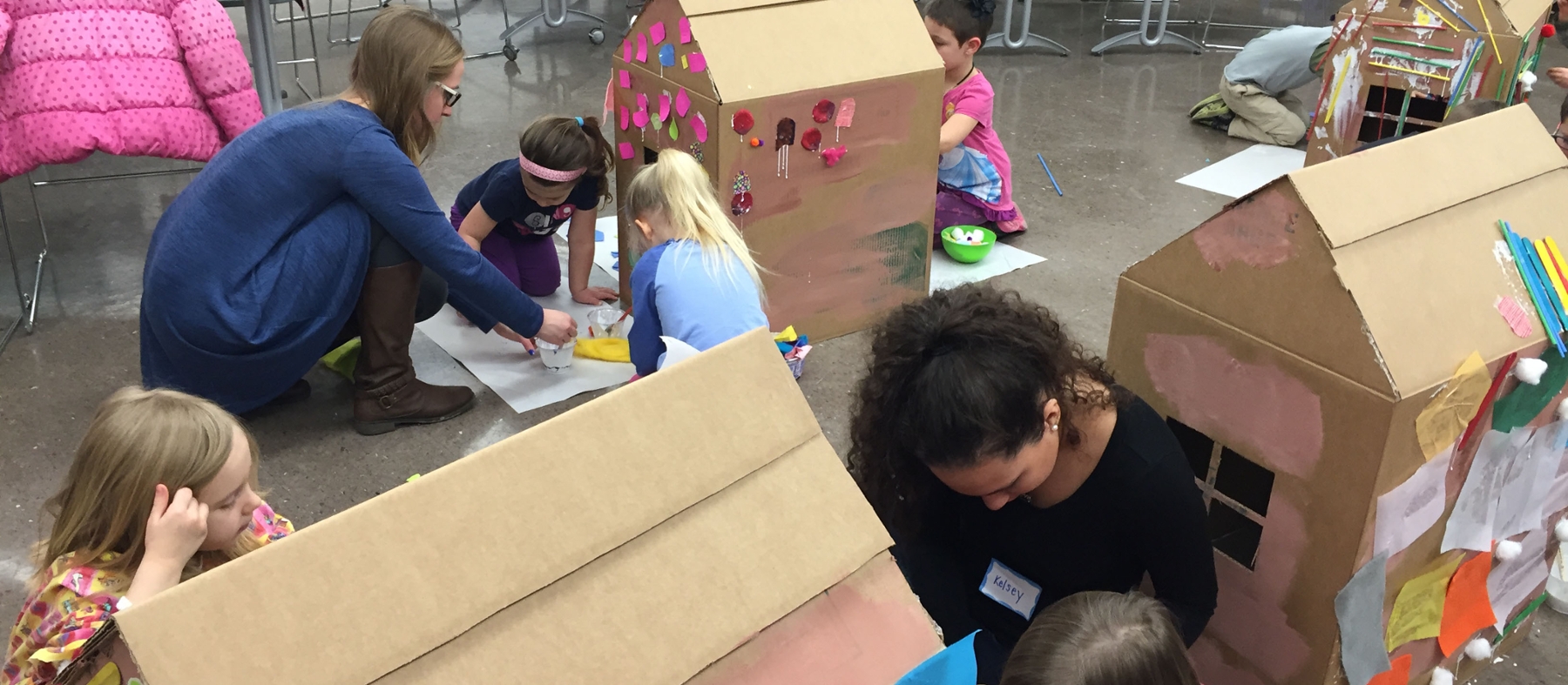 Student teachers and children paint cardboard box houses on the floor