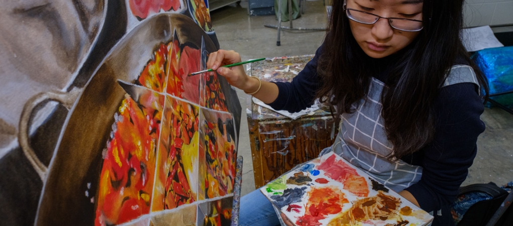 A student holding a palette looks left while working on a painting