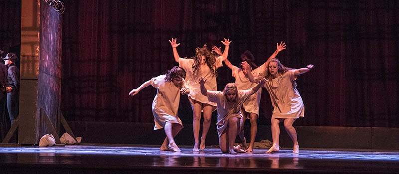 Five dancers with arms outstretched strike a pose onstage