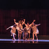 Four dancers pose with outstretched arms onstage, as another crouches in the center