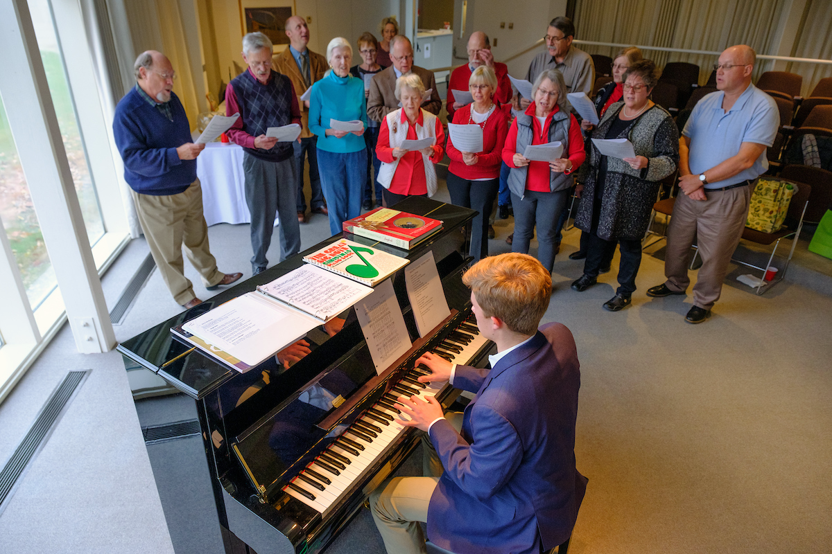 People holding song sheets sing carols near the piano as Jens Bartel plays
