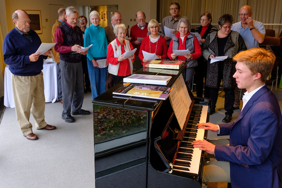 People holding song sheets sing carols near the piano as Jens Bartel plays