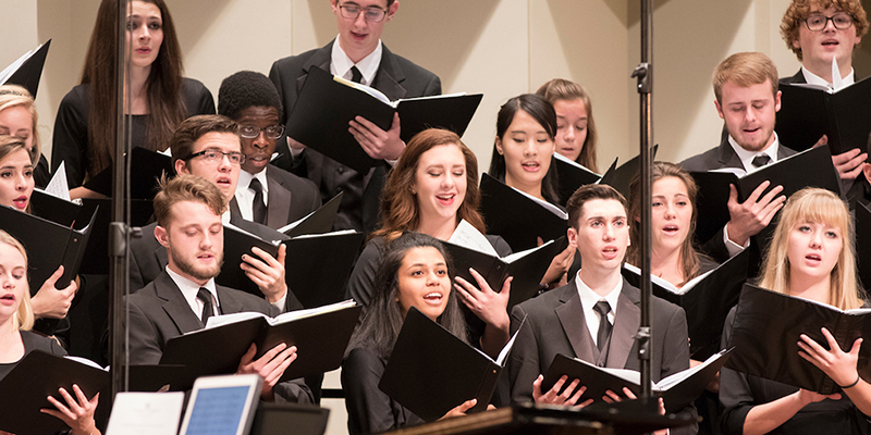  Men and women in the Collegiate Chorale hold folders and sing in concert at Hall Auditorium