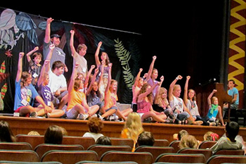 Children rehearsing stage show, arms in the air