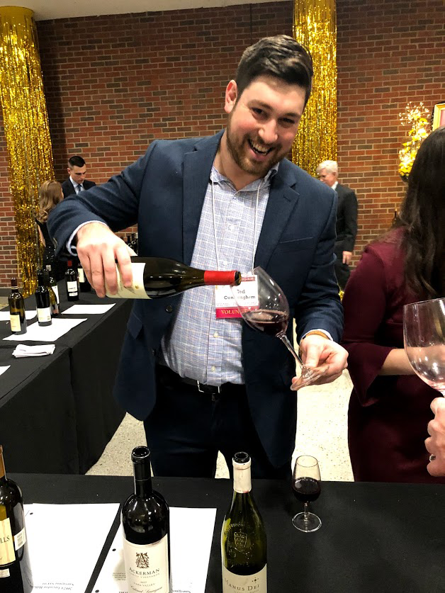 A smiling man pours wine