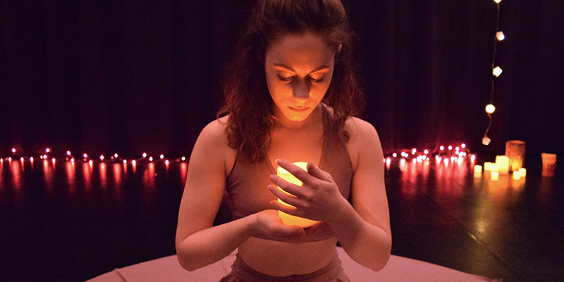 A woman gazes at a lit candle in a scene from an IAS production