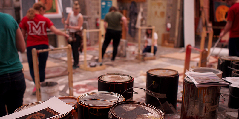  Cans of paint in foreground, with students painting scenery in background