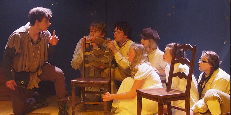 In a scene from Peter Pan, Peter speaks to a gathering of children crouching behind chairs