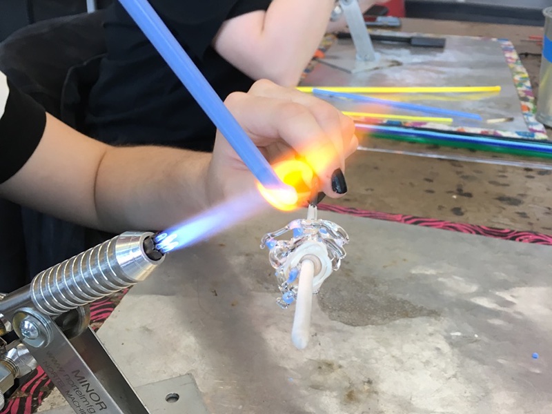 student using a torch to shape a glass bead