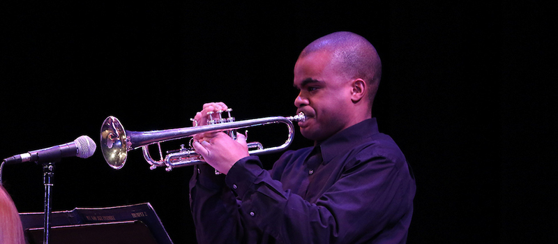 student playing the trumpet into a microphone on stage