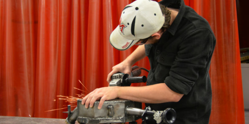 Male student using a grinder on metal in a lab