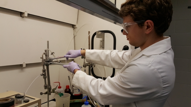 Male student wearing PPE while working under a fume hood