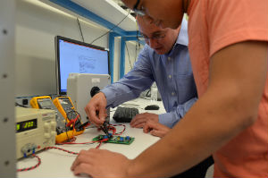 A faculty member and student work on a PCB