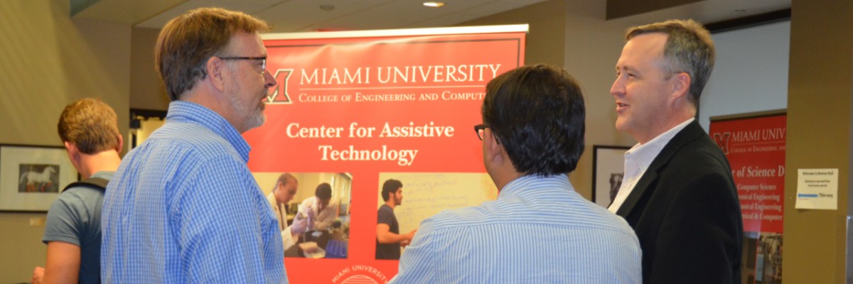 Tim Cameron, Kumar Singh, and a Mechanical and Manufacturing Engineering alum, conversing in front of a Center for Assistive Technology banner.