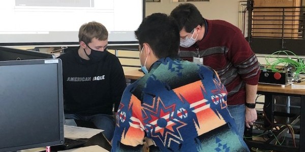 An instructor and two students peering closely at something