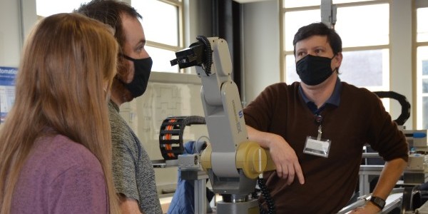 An instructor talking with two students around a machine