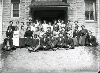 Students sitting and standing in front of a building.