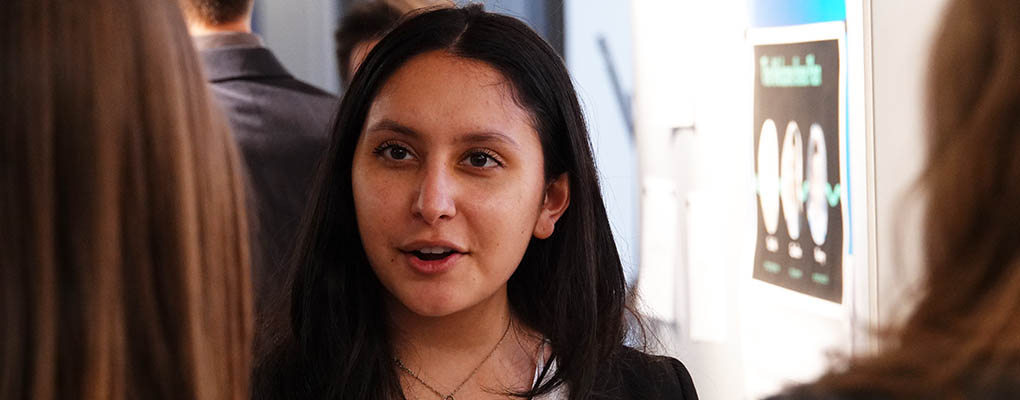 Student talks to visitors at poster presentation