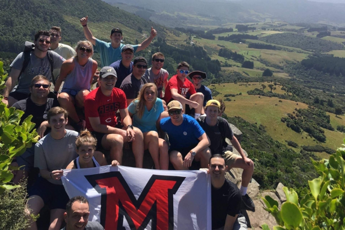 Students on a study abroad program pause to pose with a Miami flag on a mountain