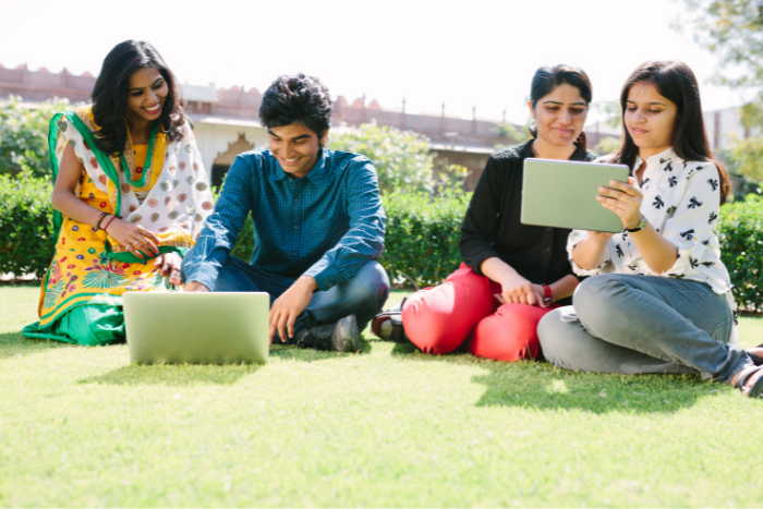 Smiling students sitting on the grass with laptop computers