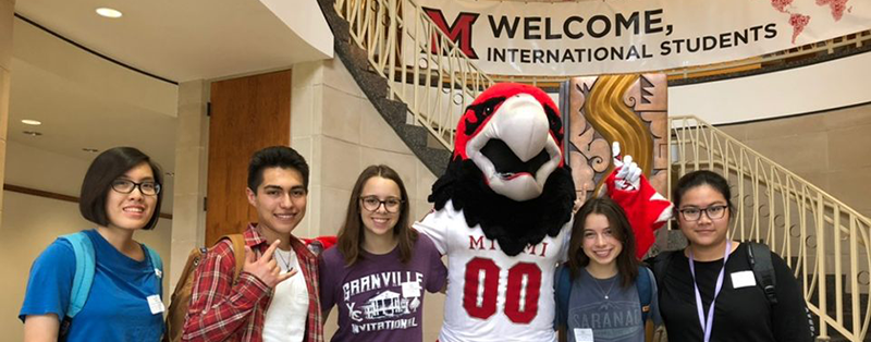  Students pose with Miami mascot Swoop in front of welcome sign for international students