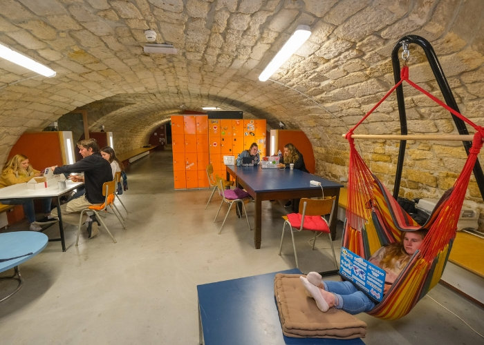 many students studying in the cave: group of 3 at table, group of 2 at another table, one in a hammock with feet propped up
